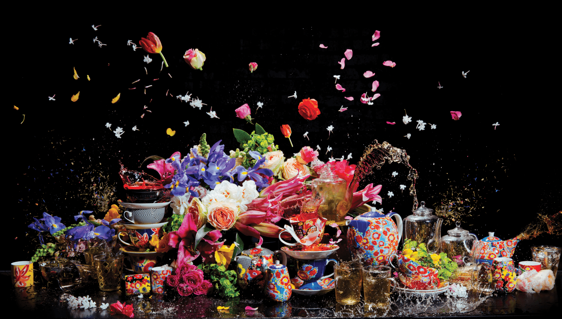 Stack of colourful tea pots, tea cups, flowers and tea leaves on a table