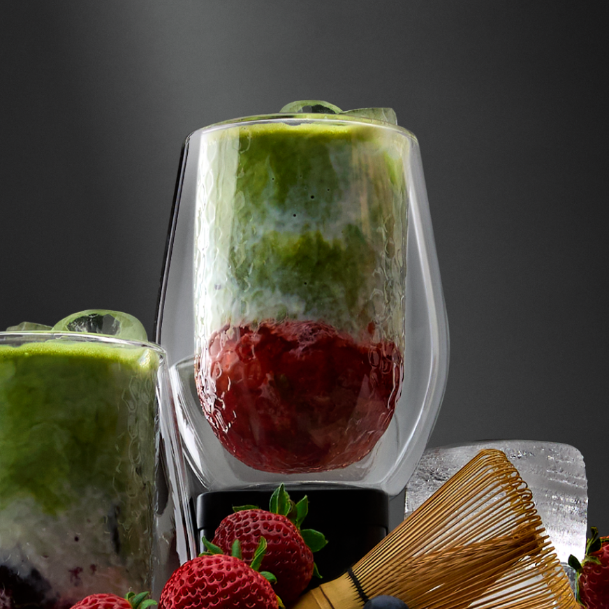 Strawberry and blueberry matcha lattes surrounded with fresh strawberries and blueberries