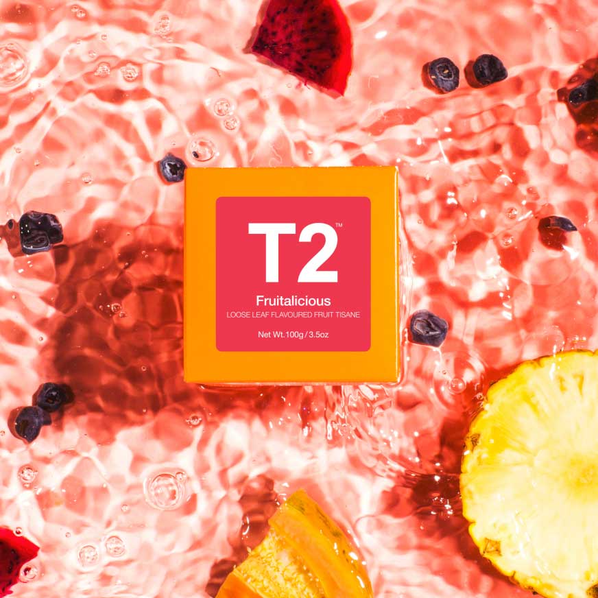 A box of T2 Fruitalicious Tea sitting in a shallow bath of mixed fruits